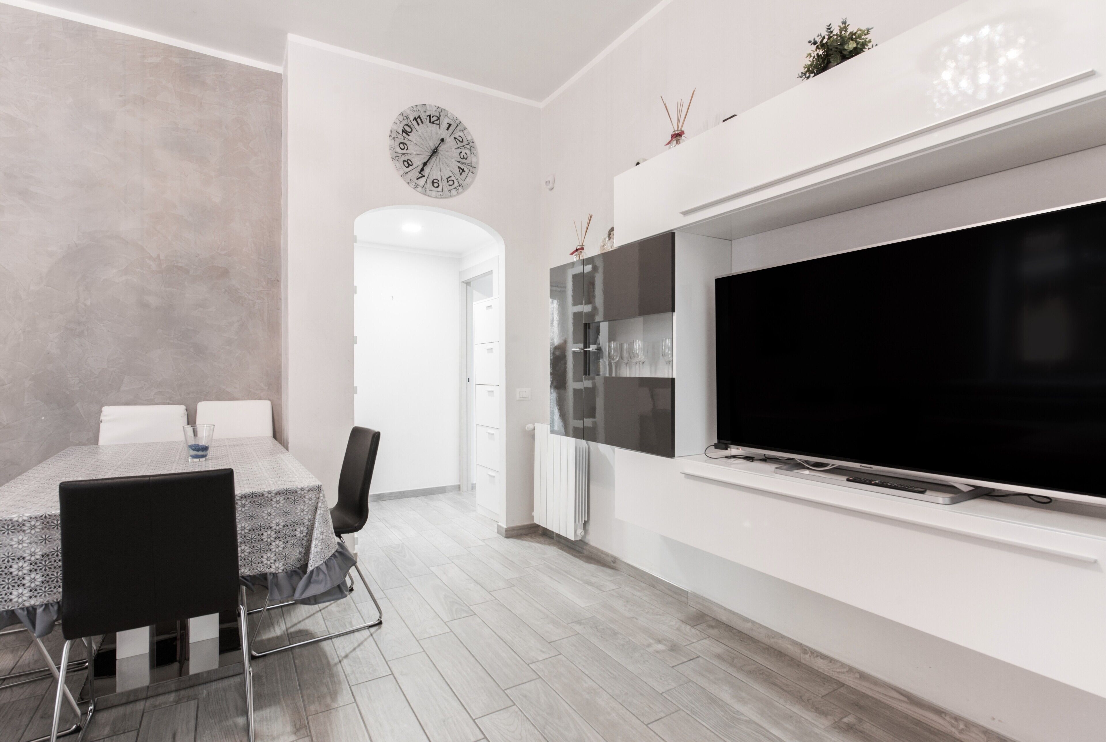 Un salon moderne doté d’un téléviseur à écran plat, d’un coin repas avec une table et des chaises, et d’une cuisine équipée d’un réfrigérateur et d’une horloge murale.