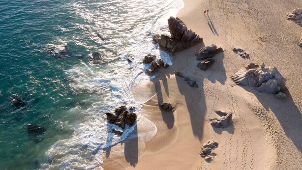Vista aérea de uma praia com formações rochosas e água azul cristalina.