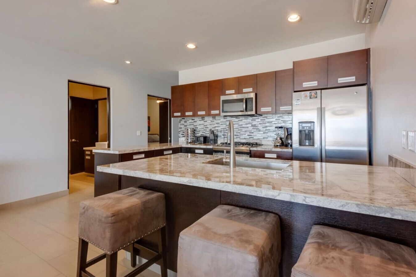 A modern kitchen with a central island, stainless steel appliances, and a tiled backsplash.