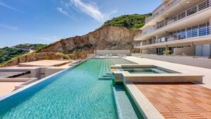 Um hotel moderno com uma grande piscina ao ar livre, um terraço escalonado e vista para o penhasco.