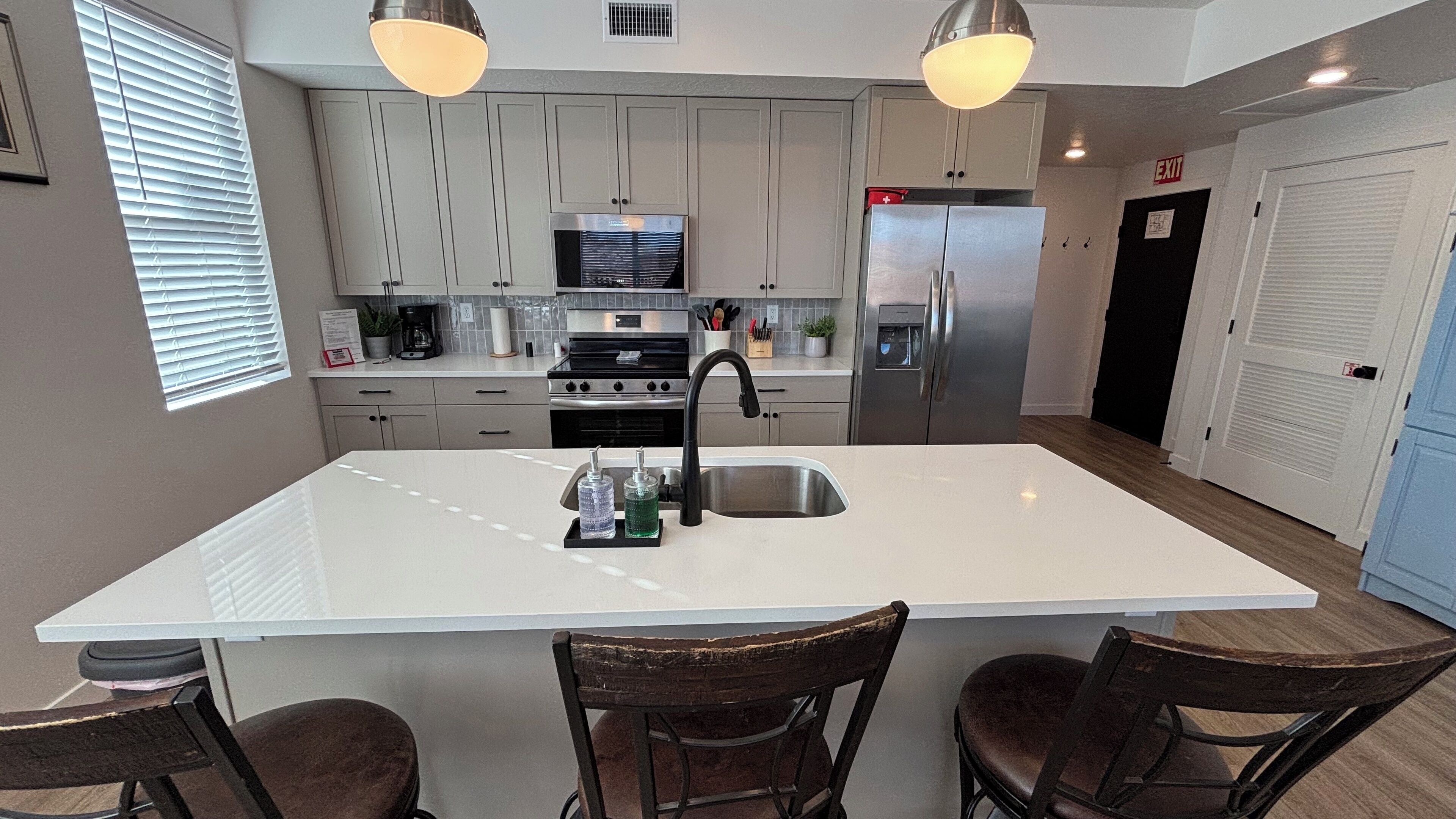 Cozinha moderna com ilha central, eletrodomésticos de aço inoxidável e iluminação pendente.