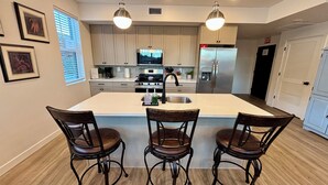 Cozinha moderna com ilha central, banquetas, eletrodomésticos de aço inoxidável e iluminação pendente.