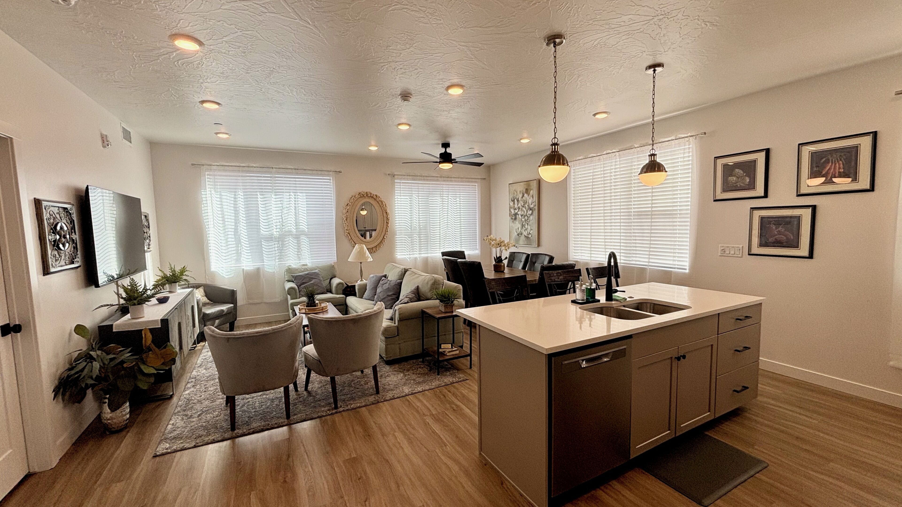 A modern kitchen with a central island, dining area with chairs, and a living room with sofas.