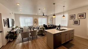 A modern kitchen with a central island, dining area with chairs, and a living room with sofas. - Desert Retreat w/Marvel Themed Bedroom (Hurricane)
