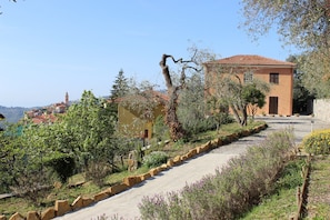 A hillside property with a paved path, a building with a red-tiled roof, and a view of a distant town.