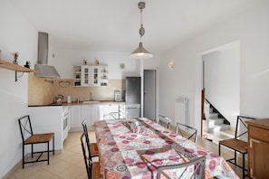 A modern kitchen with white cabinets, a stainless steel range hood, and a dining area with a patterned tablecloth.