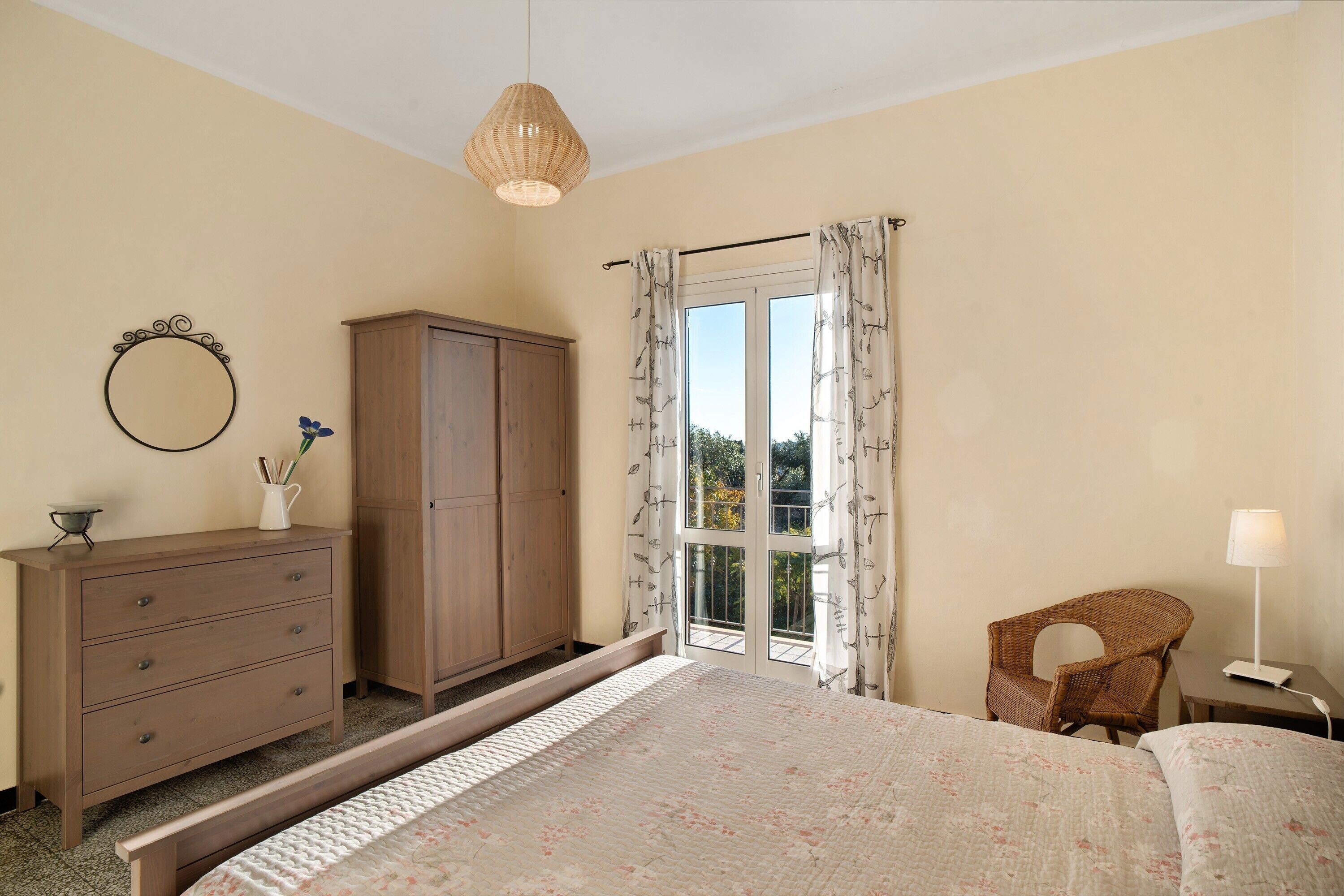 Une chambre à coucher comprenant un lit, une commode, une chaise, une lampe, une fenêtre avec des rideaux et un luminaire suspendu.