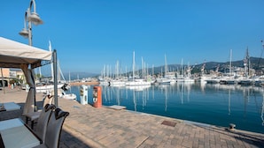 A marina with boats docked, a paved walkway, and a covered seating area.
