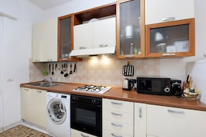 A compact kitchen with a gas stove, oven, washing machine, microwave, and a sink. - Apartment 'Leo Genova Aeroporto' with Wi-Fi (Genova)
