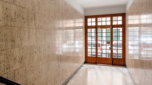 A hallway with marble walls, a wooden door with glass panels, and a view of parked cars outside.