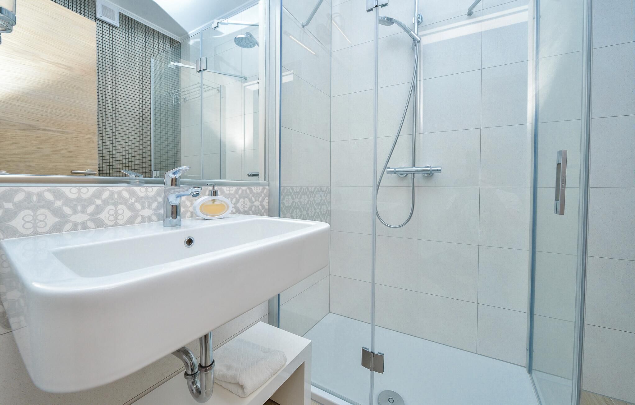 Een moderne badkamer met een witte wastafel, een douchecabine van glas en een spiegel.