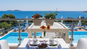 A balcony with a pool view, a table with a tray of cookies, cups, and a vase with flowers. - Nice apartment in Rogoznica with sauna (Rogoznica)