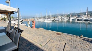 Un puerto deportivo con barcos amarrados, una zona de estar cubierta y un cielo azul despejado.