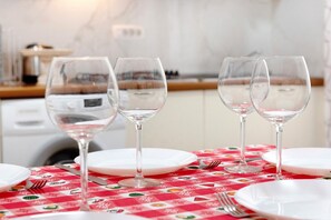 Une table à manger avec quatre verres à vin et des assiettes, une nappe à carreaux rouges et, au fond, une cuisine.