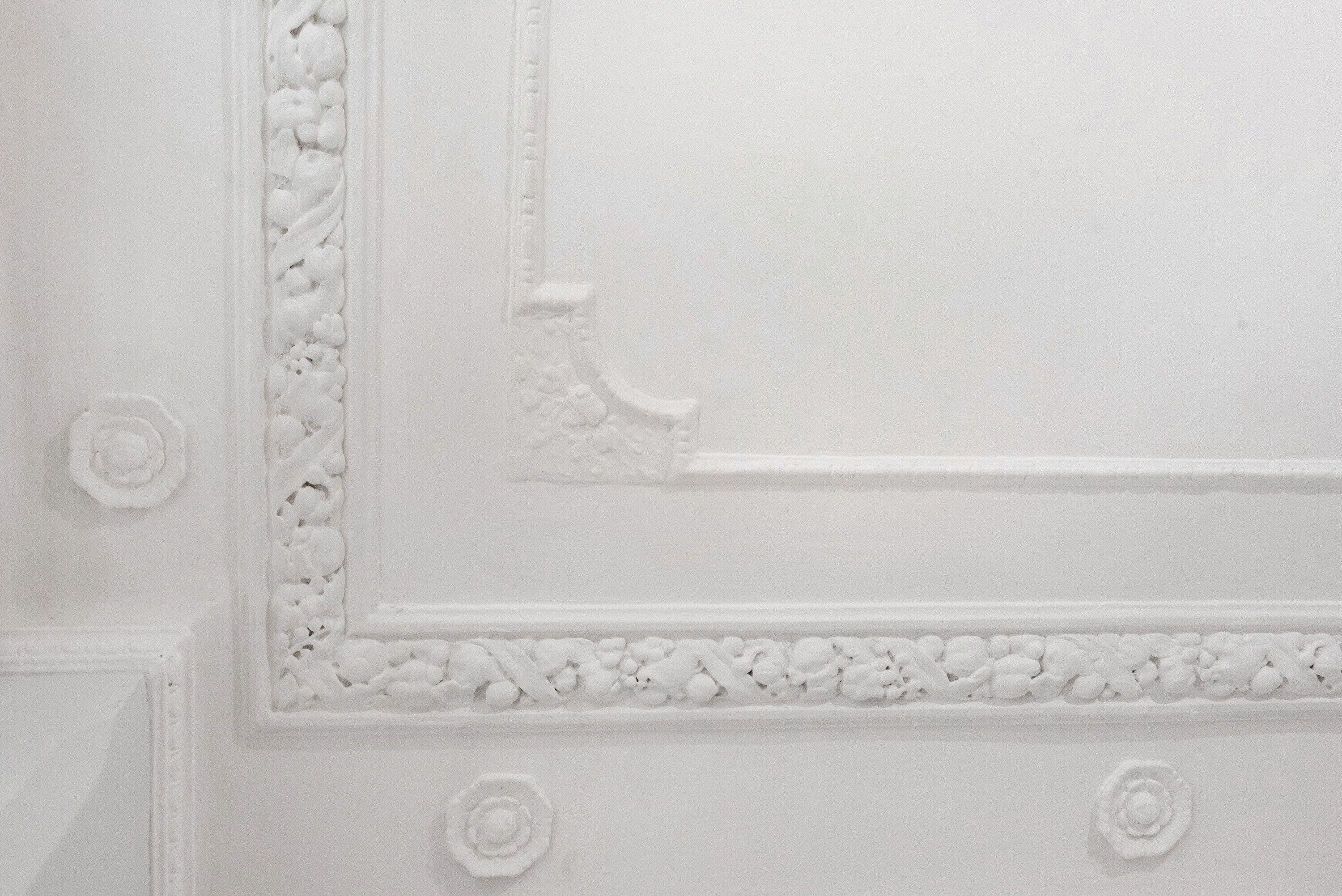 A white wall with intricate molding and decorative elements.