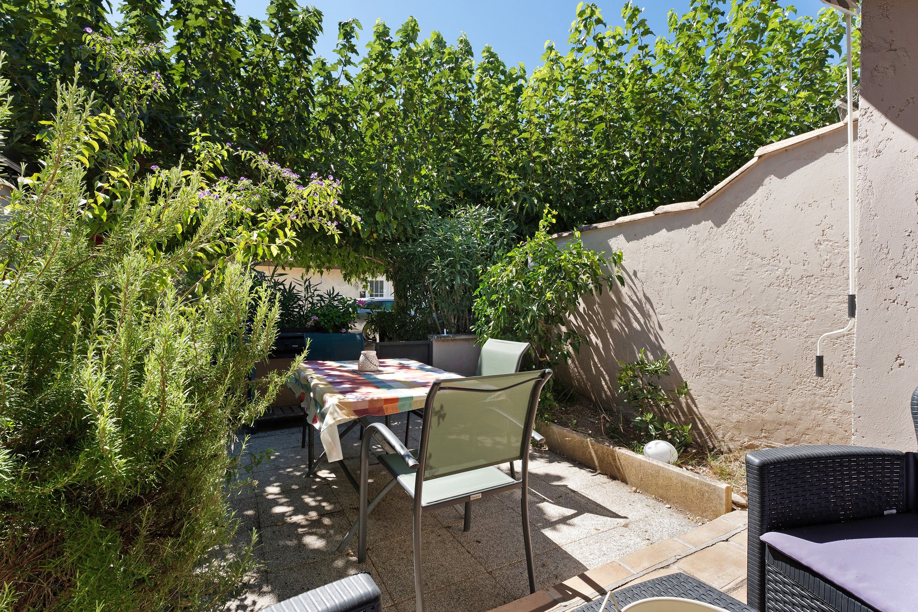 An outdoor patio area with a table and chairs, surrounded by greenery and a wall.
