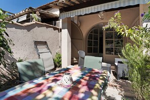 An outdoor seating area with a table set for two, surrounded by wicker chairs and a patterned tablecloth.