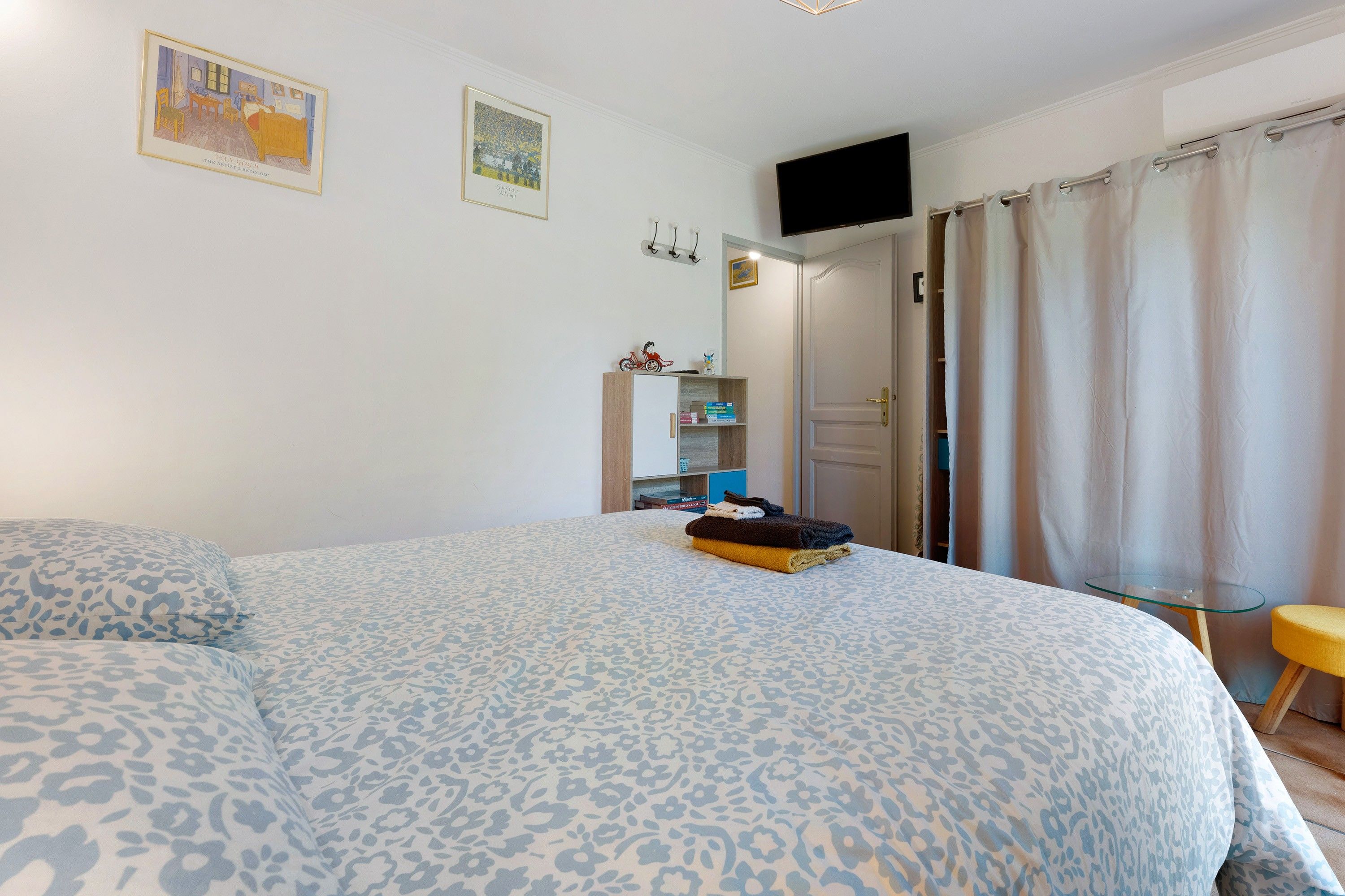 Une chambre avec un grand lit, un téléviseur fixé au mur et une porte donnant sur une autre pièce.