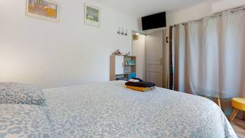 Une chambre avec un grand lit, un téléviseur fixé au mur et une porte donnant sur une autre pièce.