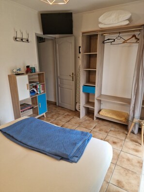 A bedroom with a bed, a wardrobe, a shelf with books, and a door leading to another room.