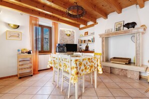 A dining area with a table set for four, a kitchen area with a microwave, and a fireplace with a mantel. - Holiday Home 'Lago' with Lake View and Private Terrace (Brenzone sul Garda)