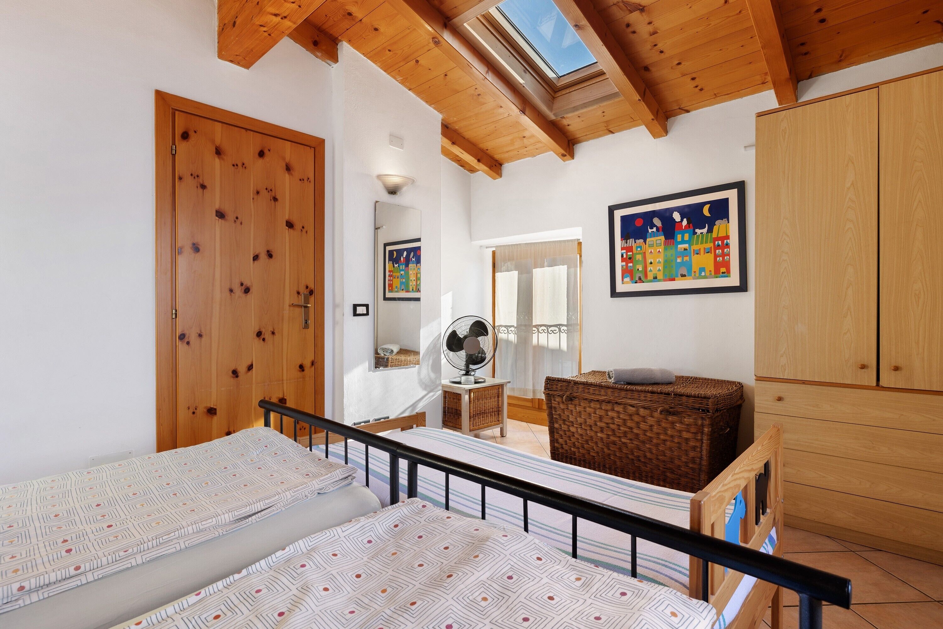 Ein Schlafzimmer mit zwei Betten, Holzbalkendecke, Dachfenster, einem Spiegel, einem Ventilator und einem Korbwannenkorb.