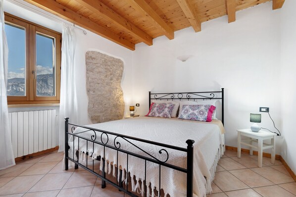 A bedroom with a bed, a stone wall, a window, and a bedside table.