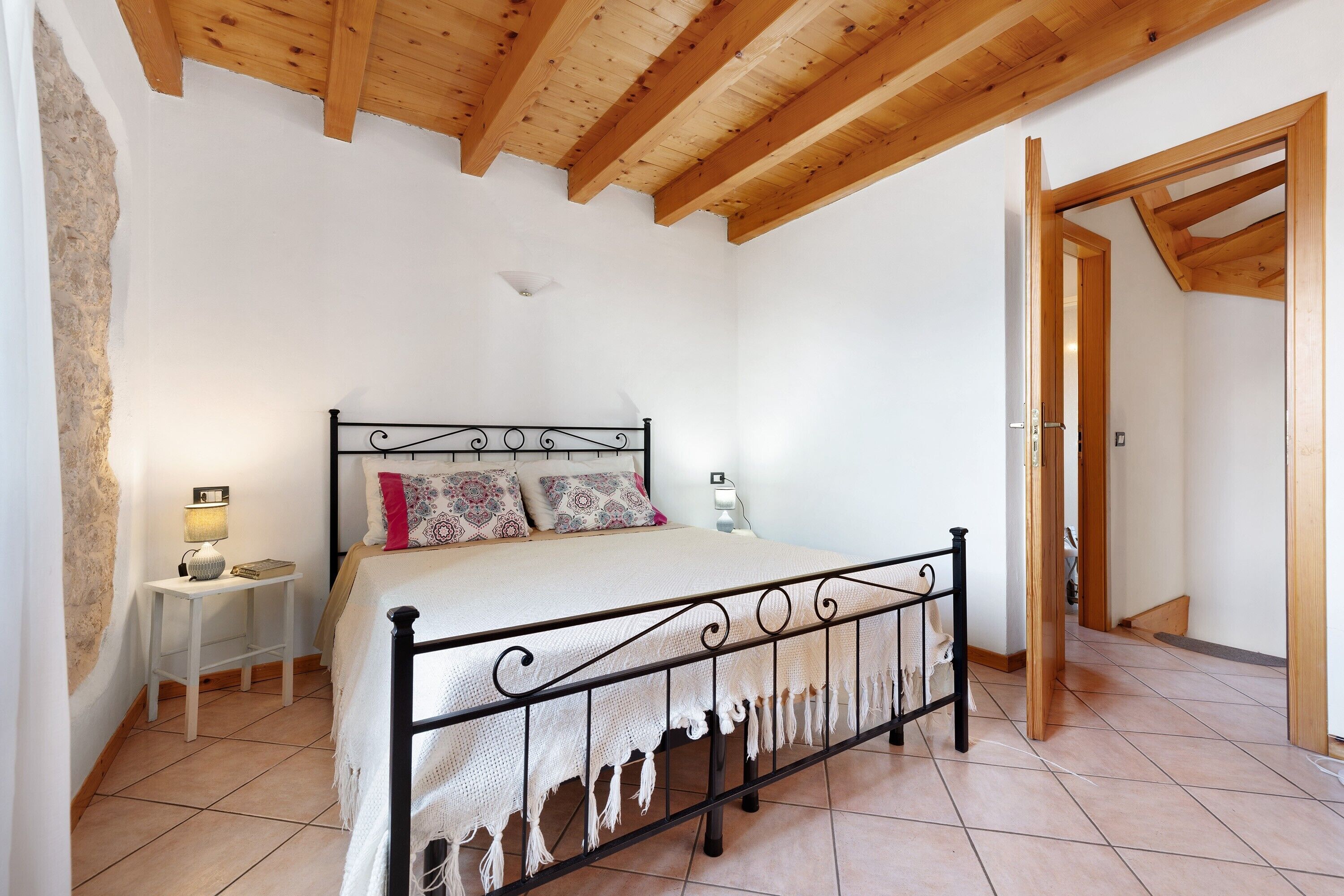 A bedroom with a bed, bedside table, lamp, and a wooden ceiling.