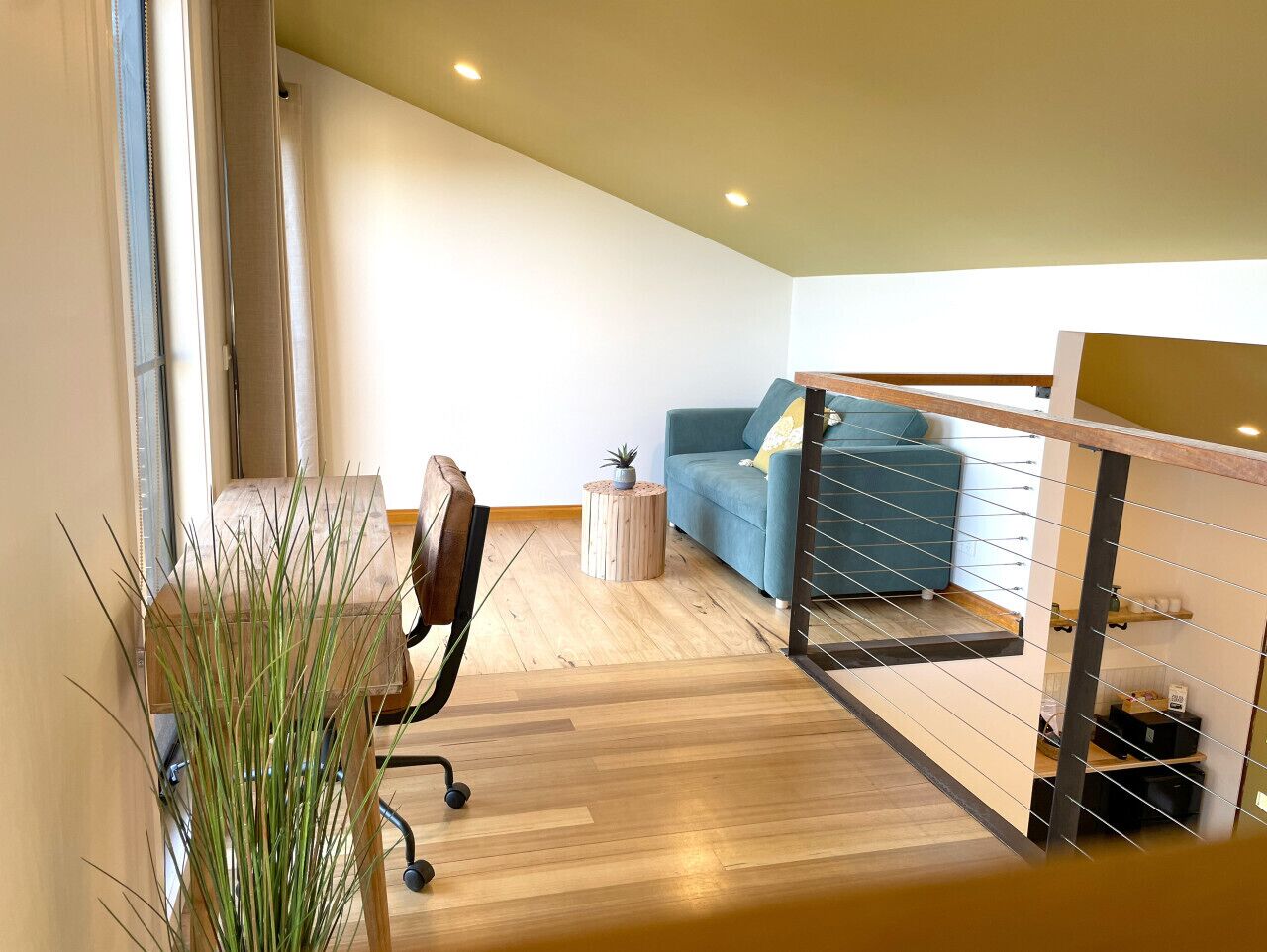 Ein modernes Wohnzimmer mit Holzboden, einem blauen Sofa, einem kleinen runden Tisch und einem Blumentopf.