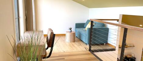 Ein modernes Wohnzimmer mit Holzboden, einem blauen Sofa, einem kleinen runden Tisch und einem Blumentopf.