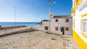 A cobblestone street leading to a beach, a white building with yellow trim, and a clear blue sky.