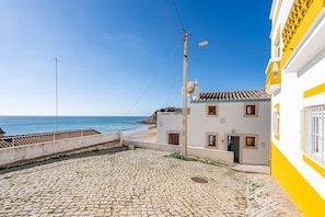 A cobblestone street leading to a beach, a white building with yellow trim, and a clear blue sky.