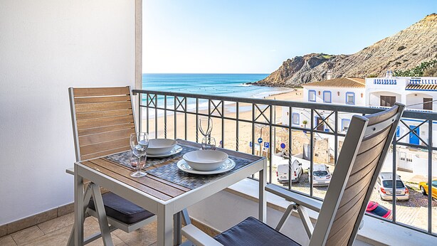 A balcony with a table and chairs, overlooking a beach and rocky terrain.