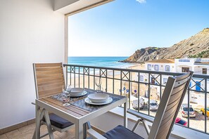 A balcony with a table and chairs, overlooking a beach and rocky terrain. - Apartment 'Beach Apt 1' with Sea View, Wi-Fi and Air Conditioning (Burgau)