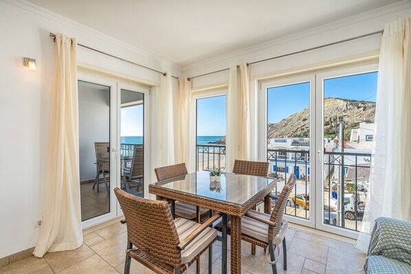 Un balcon avec une table en verre et des chaises en osier, donnant sur une zone côtière.