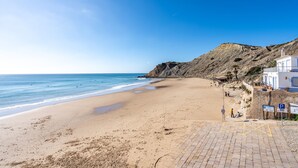 A beach with a paved walkway, a rocky cliff, and a building with a blue sign.
