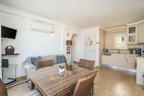 A compact living space with a dining table, wicker chairs, a sofa, a TV, and a kitchen area.