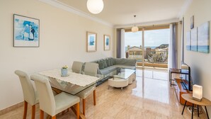 A modern living room with a glass dining table, a sofa, and a view of the sea. - Apartment 'Brightness Comfort In Burgau' with Sea View, Wi-Fi and Air Conditioning (Burgau)