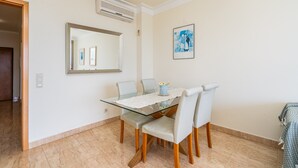 A dining area with a glass table, four chairs, a ceiling light, an air conditioner, and a framed picture on the wall. - Apartment 'Brightness Comfort In Burgau' with Sea View, Wi-Fi and Air Conditioning (Burgau)