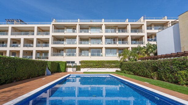 A swimming pool with a tiled deck, surrounded by a hedge and a multi-story building with balconies. - Apartment 'Brightness Comfort In Burgau' with Sea View, Wi-Fi and Air Conditioning (Burgau)