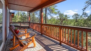 Una terraza de madera con barandilla, una mesa y dos mecedoras.