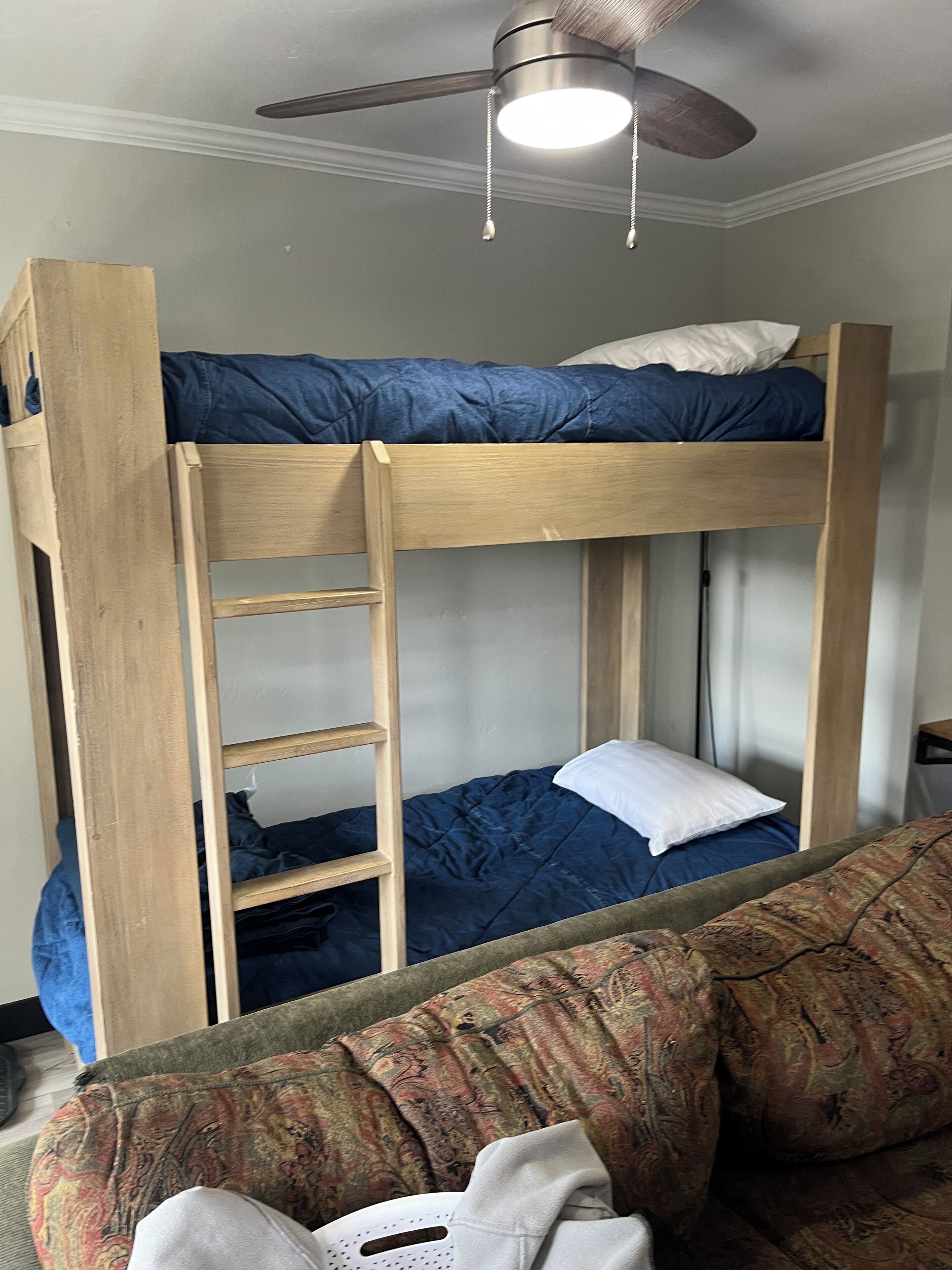 Een stapelbed met een houten ladder, een plafondventilator en een gestreept bedbankje op de voorgrond.