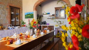 A long dining table set with various dishes and drinks, a brick wall, and a painting on the wall. - Villa Podere del Papa by MMega (Pienza)