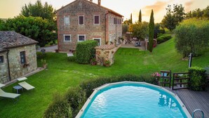 A stone building with a swimming pool, surrounded by a well-maintained lawn and garden. - Villa Podere del Papa by MMega (Pienza)