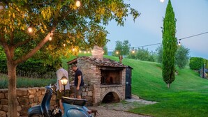 A stone outdoor kitchen with a chimney, a scooter, and a tree with string lights. - Villa Podere del Papa by MMega (Pienza)