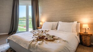 Ein Hotelzimmer mit einem großen Bett, zwei Nachttischen mit Lampen, einer Frühstücksplatte und Blick auf eine grüne Landschaft durch das Fenster.