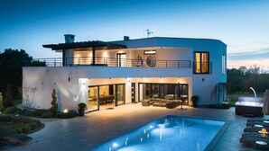 Ein modernes, zweistöckiges Haus mit Swimmingpool, Sitzgelegenheiten im Freien und einem gut beleuchteten Patio.