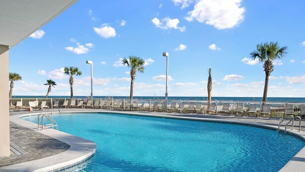 Piscina com espreguiçadeiras e palmeiras, com vista para o oceano.