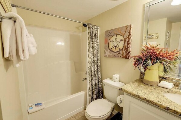 A bathroom with a bathtub, toilet, and sink. There is a towel rack with towels, a shower curtain, and a potted plant on the counter.