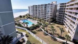 Hotel com vários andares, área de piscina, palmeiras e vista para a praia.